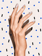 Editorial hand wearing Begin Again iridescent floral press-on nails on a blue dot patterned background