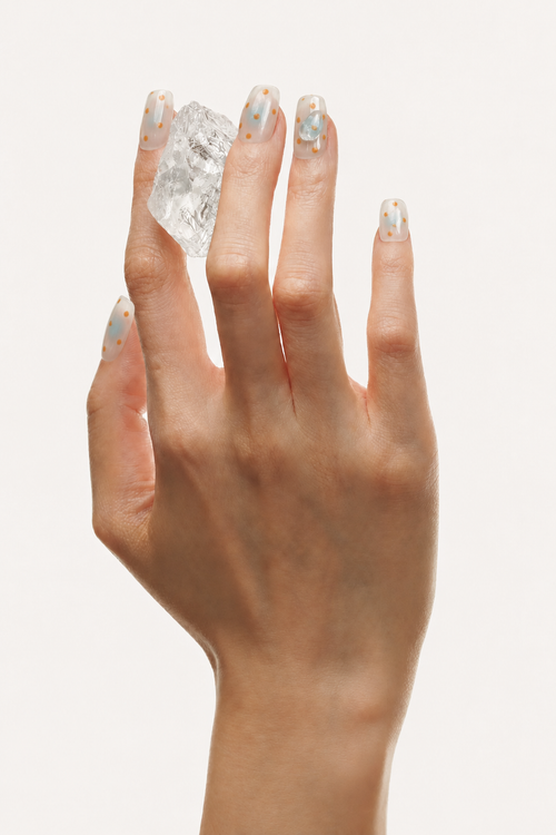Flat lay of Breathe nude aura press-on nails with orange-blue blur, dots and clear crystals
