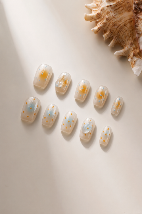 Hand wearing Breathe nude aura press-on nails with orange-blue blur, dots and clear crystals
