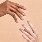 Two hands wearing Clear Mind nude-pink crystal press-on nails on a peach background