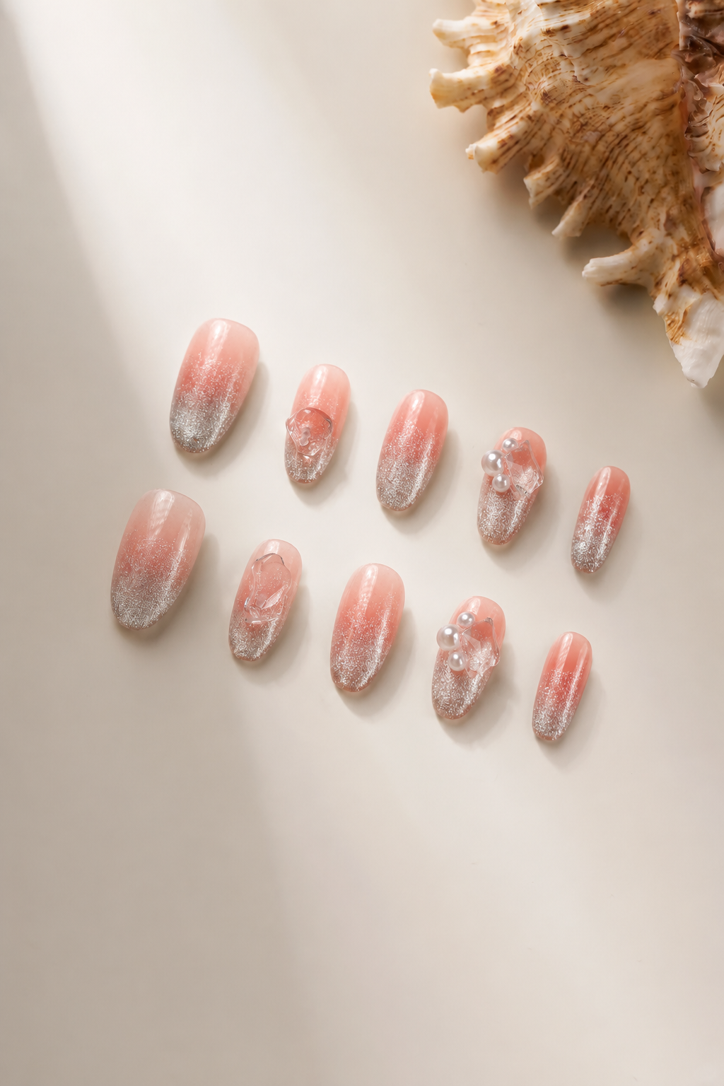 Flat lay of Clear Mind nude-pink press-on nails with silver shimmer and clear crystal accents
