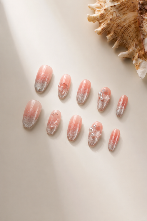 Flat lay of Clear Mind nude-pink press-on nails with silver shimmer and clear crystal accents
