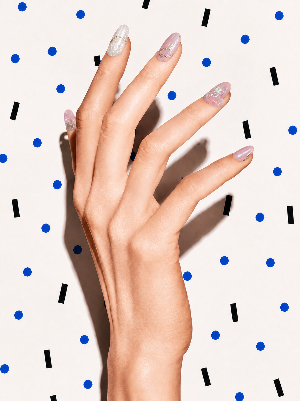 Editorial hand wearing Deep Within pink iridescent crystal press-on nails on a blue dot patterned background