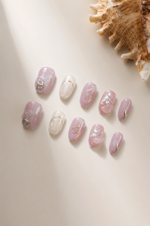 Flat lay of Deep Within pink iridescent press-on nails with gold lines and crystal shards
