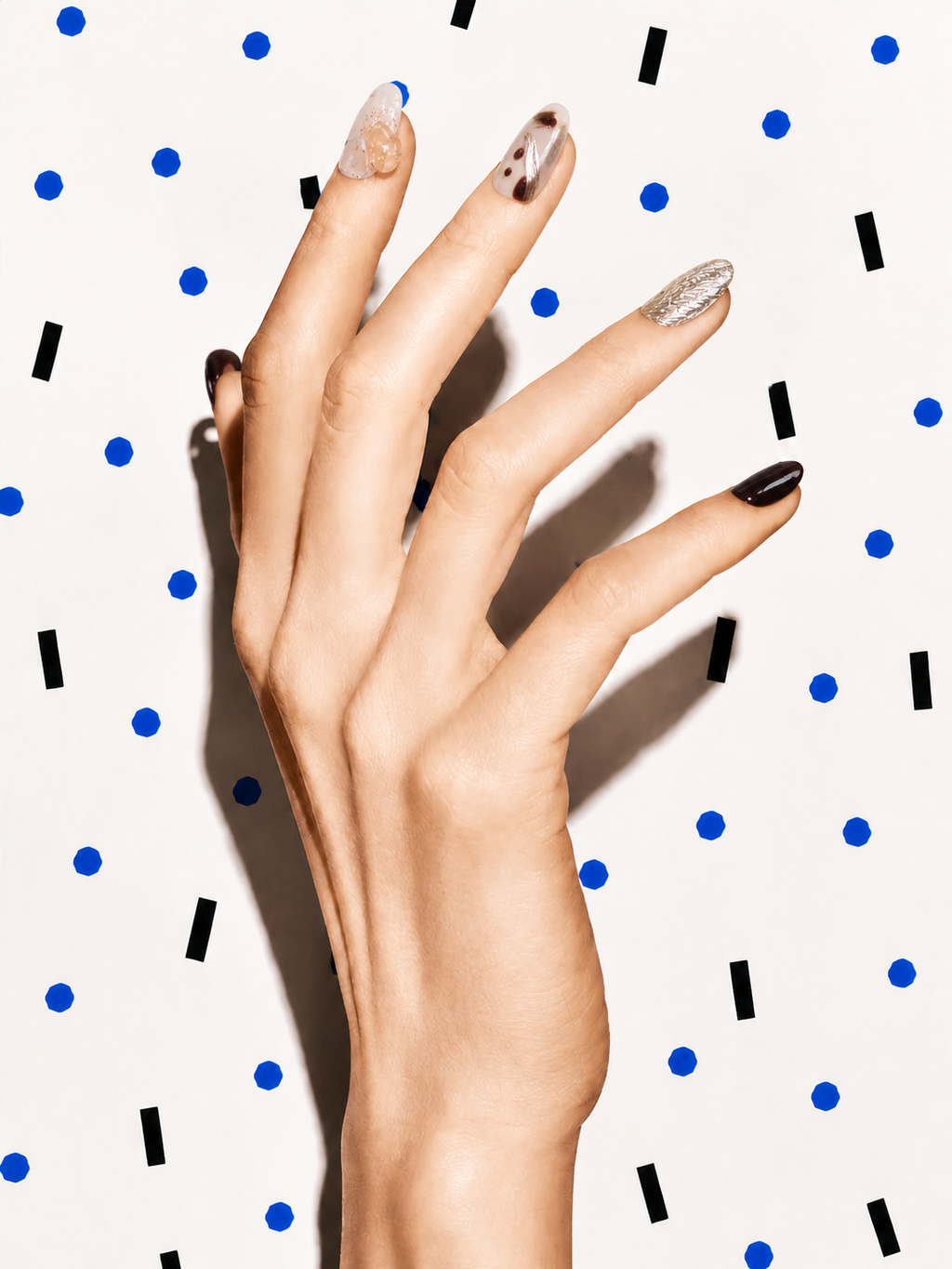 Editorial hand wearing First Light brown gold citrine press-on nails on a blue dot patterned background