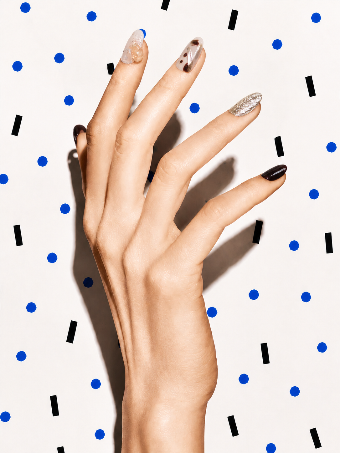 Editorial hand wearing First Light brown gold citrine press-on nails on a blue dot patterned background