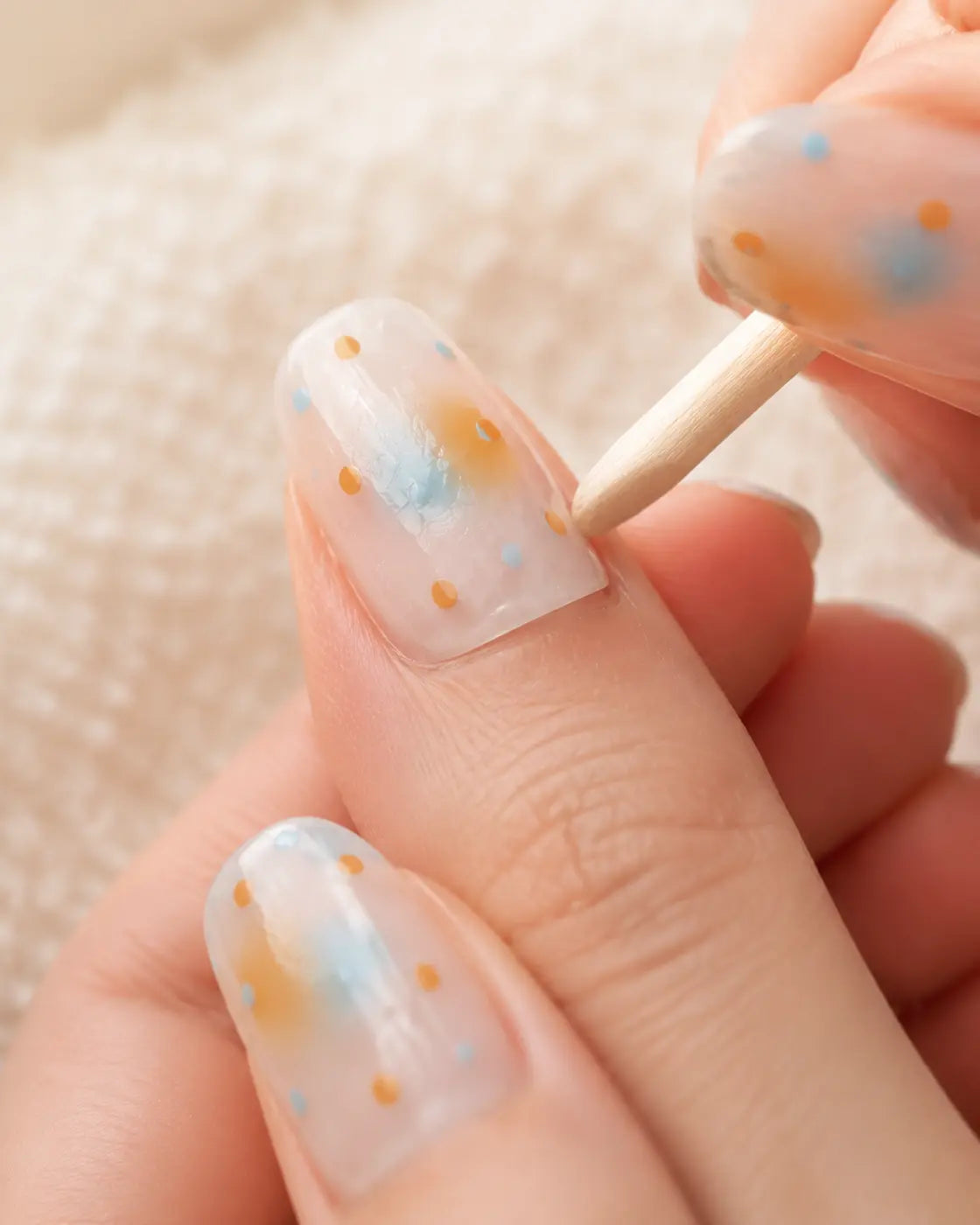 A press-on nail edge being gently tested with a wooden cuticle stick after soaking