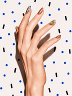 Editorial hand wearing Golden Hour bronze metallic citrine press-on nails on a blue dot patterned background