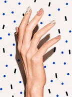 Editorial hand wearing New Sprout pink green floral press-on nails on a blue dot patterned background