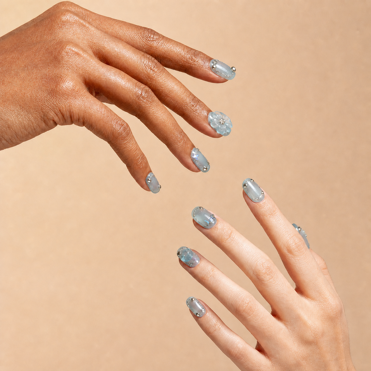 Two hands wearing Open Sky blue 3D floral crystal press-on nails on a peach background