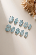 Flat lay of Open Sky blue 3D floral press-on nails with white flowers, rhinestones and aquamarine
