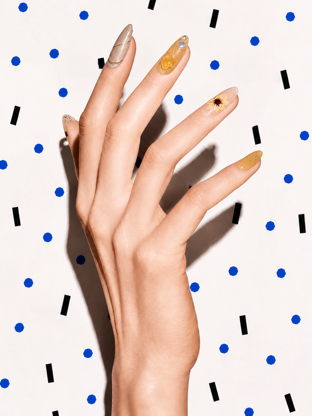 Editorial hand wearing Quiet Light amber floral crystal press-on nails on a blue dot patterned background