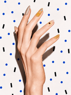 Editorial hand wearing Quiet Light amber floral crystal press-on nails on a blue dot patterned background