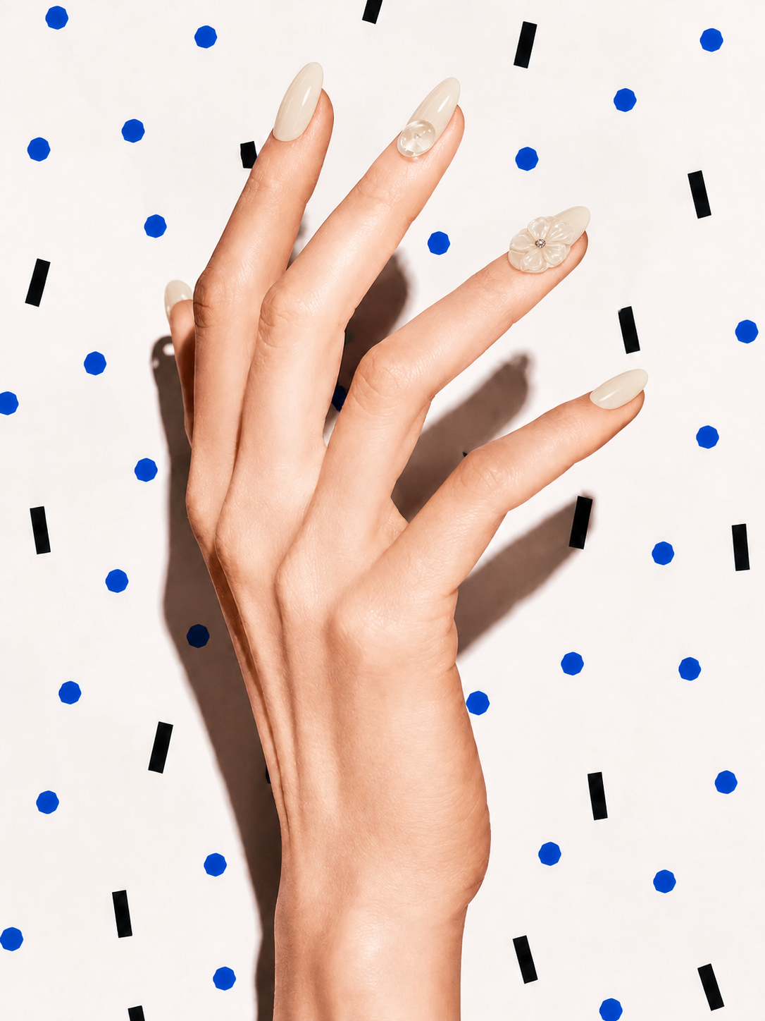 Editorial hand wearing Untangled ivory 3D floral press-on nails on a blue dot patterned background