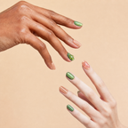 Two hands wearing With Grace peach and green crystal press-on nails on a peach background