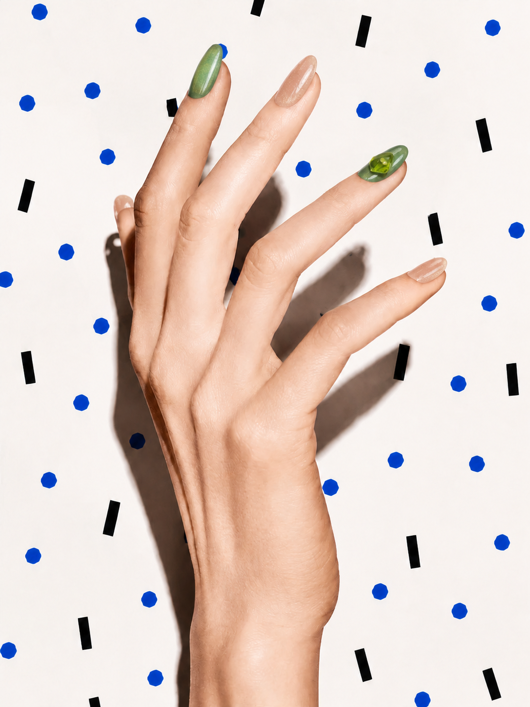 Editorial hand wearing With Grace peach and green crystal press-on nails on a blue dot patterned background